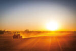 Ein Traktor fährt bei Sonnenaufgang über ein staubiges Feld. Diese Aufnahme symbolisiert die harte Arbeit und das Engagement in der Landwirtschaft, wobei Prowebco hochwertige Informationen und Produkte für landwirtschaftliche Maschinen und Baumaschinenzubehör bietet.