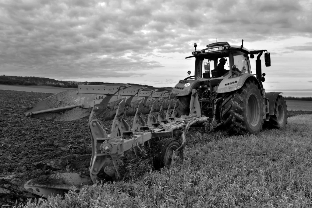 Traktor zieht einen Pflug über ein Feld unter einem bewölkten Himmel.